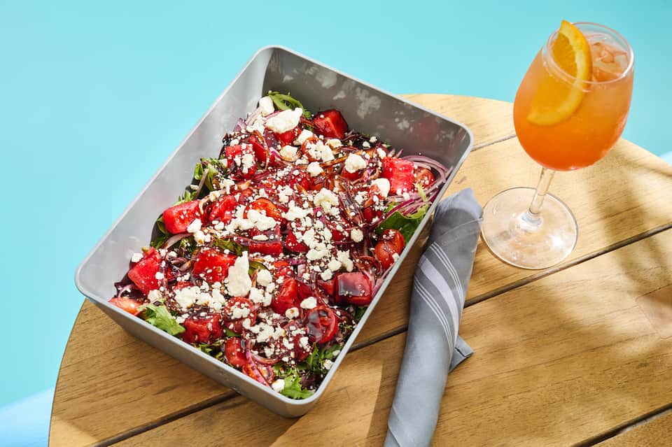 Colorful salad with feta cheese and refreshing orange beverage on a wooden table