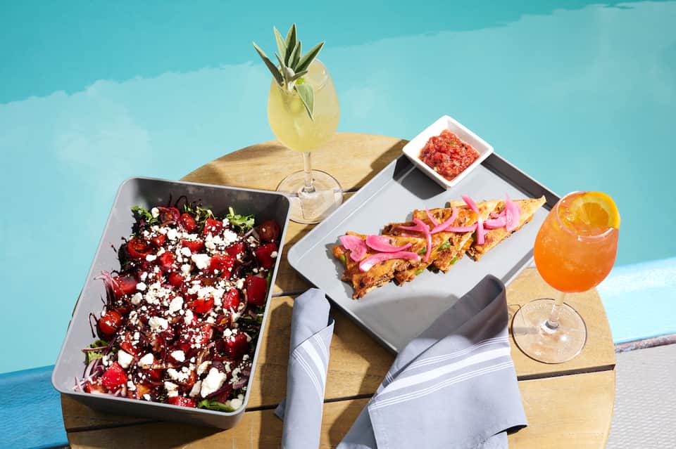 Poolside food and cocktails including salad, appetizers, and tropical drinks on table