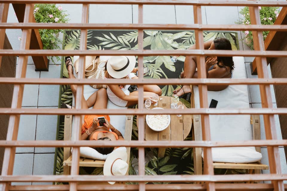 Overhead view of guests dining at wooden tables on a terrace with tropical plant patterns and palm greenery
