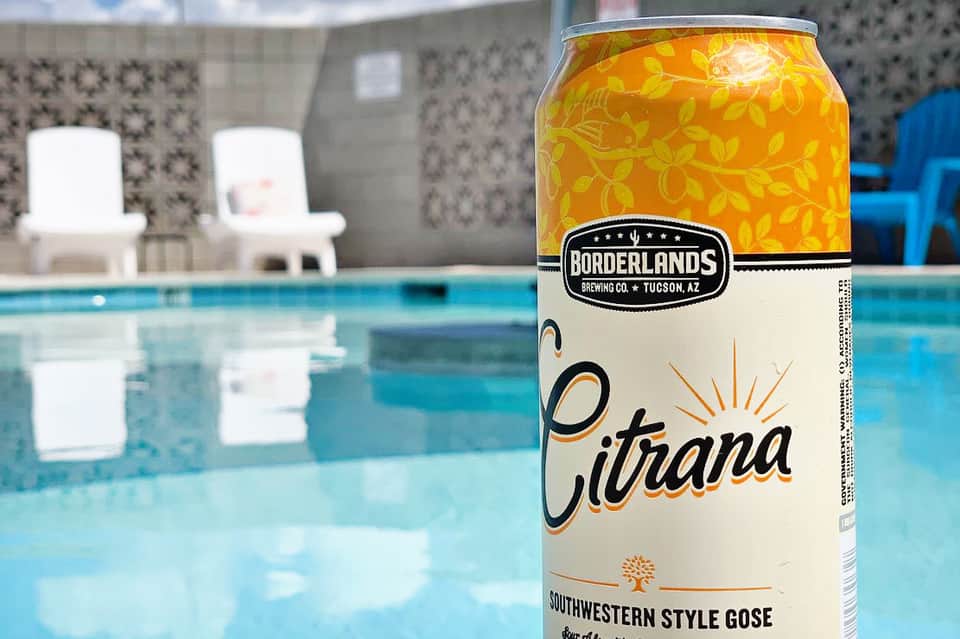 Borderlands Brewing Citrana beer can by poolside with lounge chairs and patterned walls
