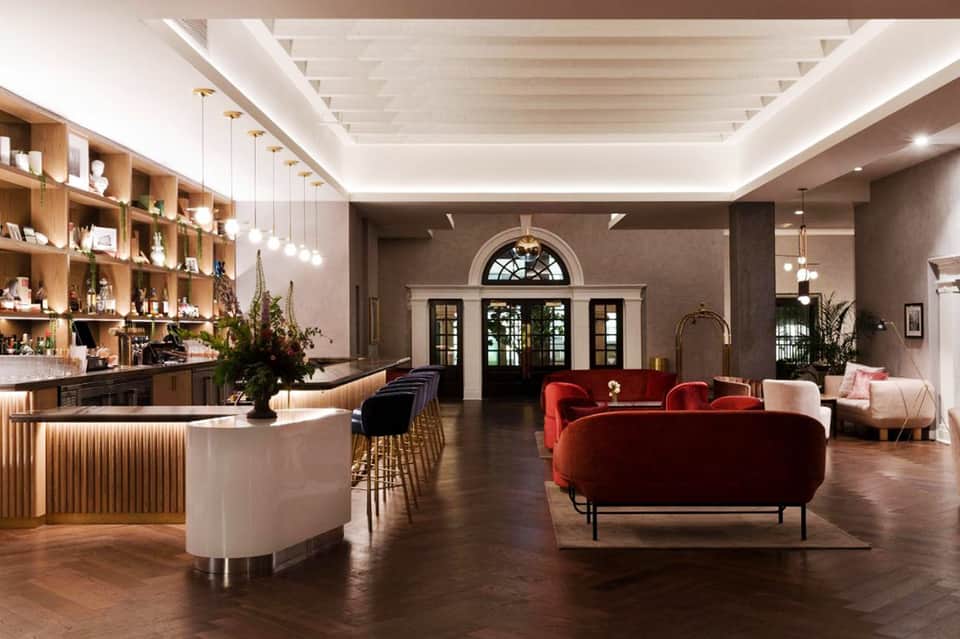 Elegant hotel lobby with red velvet sofa, wooden shelving, curved bar, and modern lighting