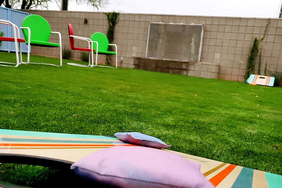 Colorful cornhole game boards on manicured green lawn with soccer goals and brick wall backdrop