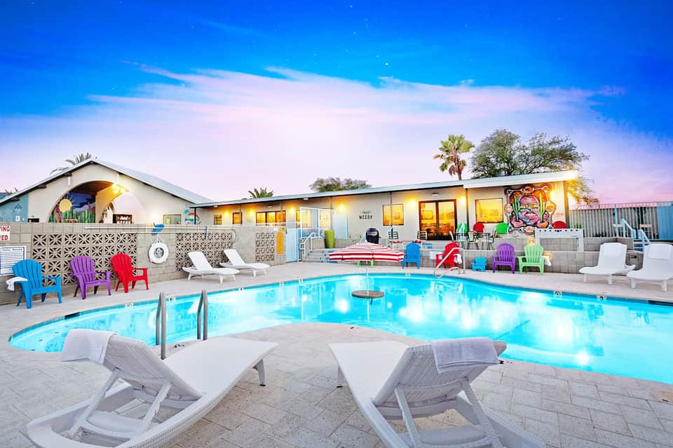 Colorful resort pool area at dusk with lounge chairs, cabanas, and illuminated buildings
