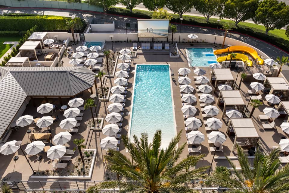 Aerial view of resort pool deck with white umbrellas, loungers, and spa facilities