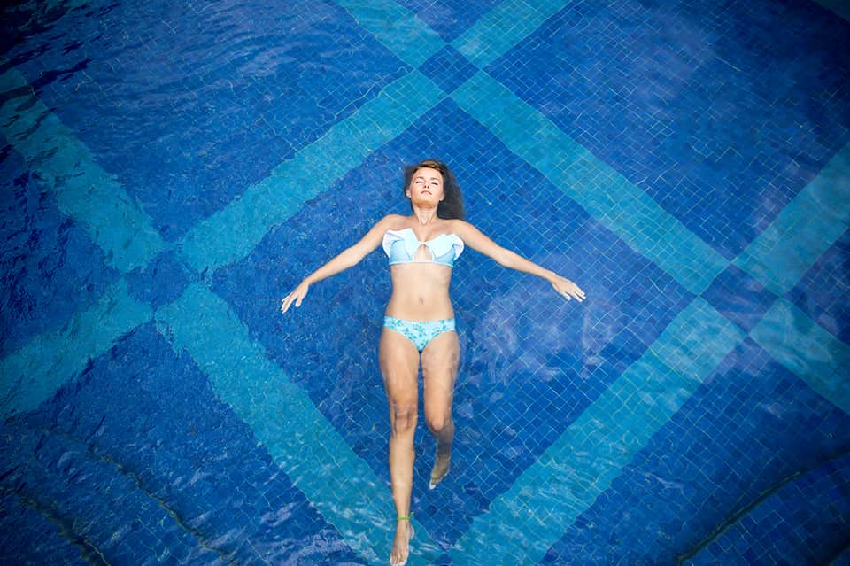 Woman floating in swimming pool wearing light blue bikini, overhead view