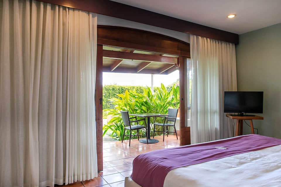 Luxury bedroom with purple bedding, terrace doors opening to ocean view patio with tropical plants