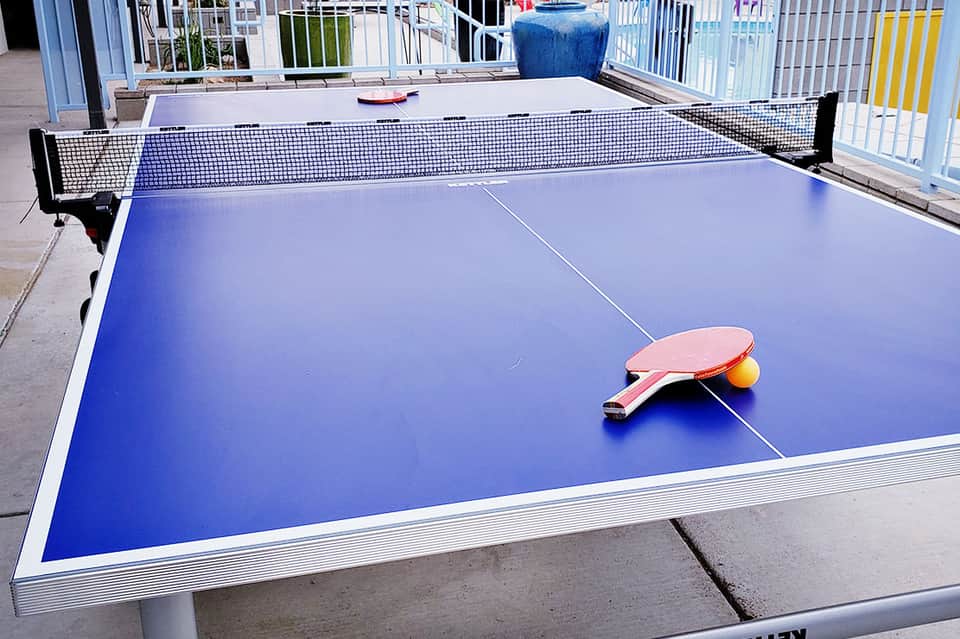Blue ping-pong table with paddle and ball in outdoor recreational area