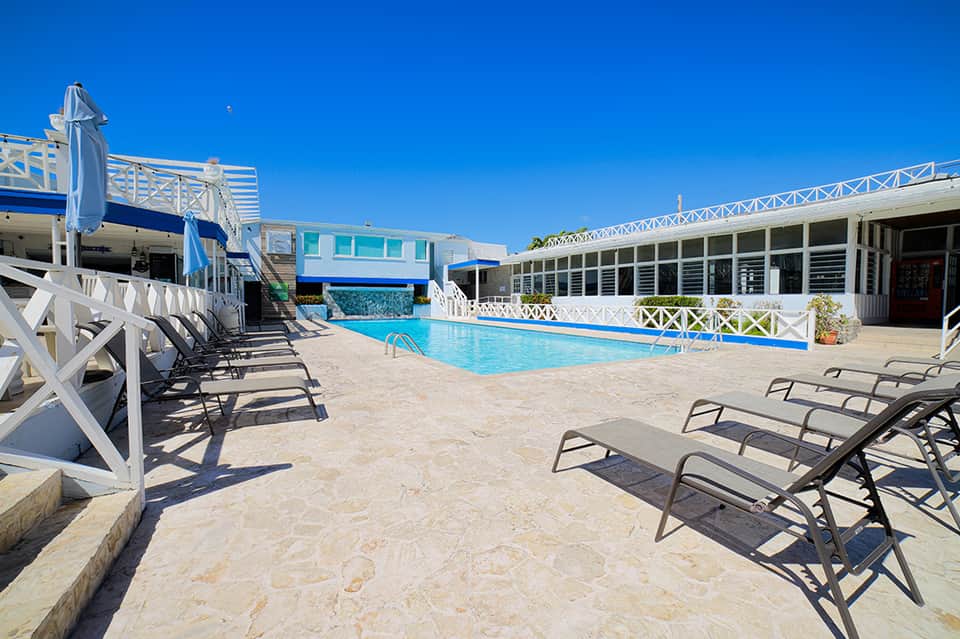 Bright blue rectangular pool with white lounge chairs and blue and white modern hotel buildings