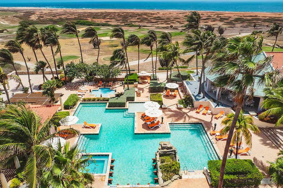 Aerial view of beachfront resort with turquoise pools, palm trees, and ocean coastline