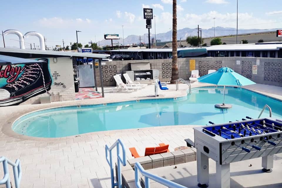 Bright turquoise swimming pool with blue umbrella, lounge chairs, and foosball table on desert landscape