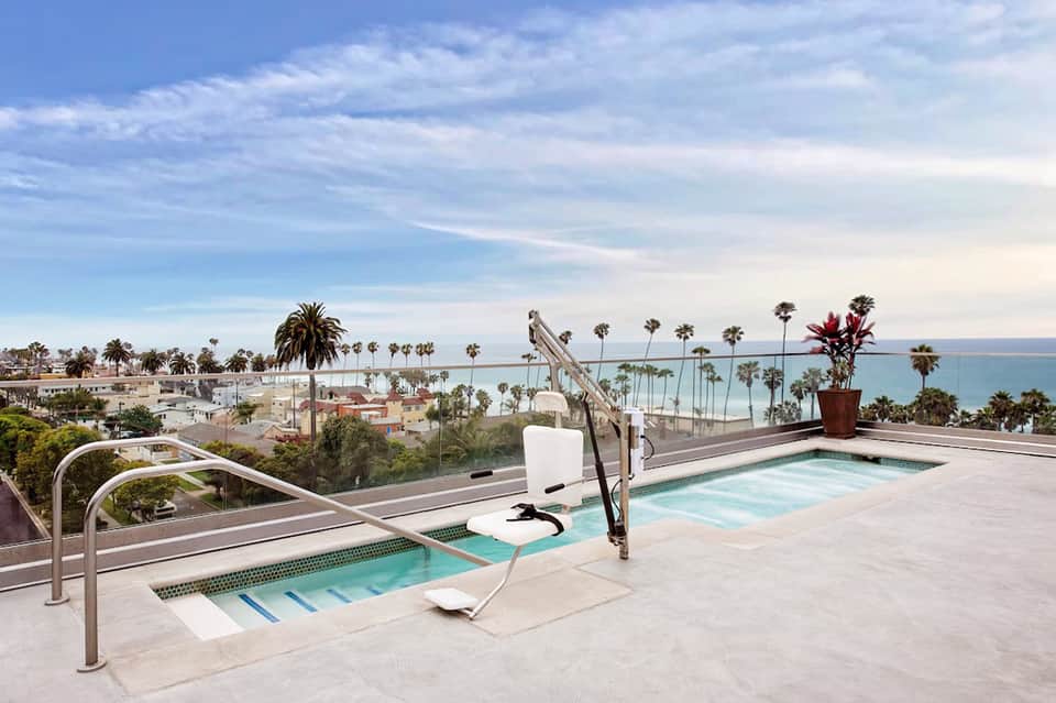 Rooftop spa area with hot tubs overlooking palm-lined coastal town and turquoise ocean waters