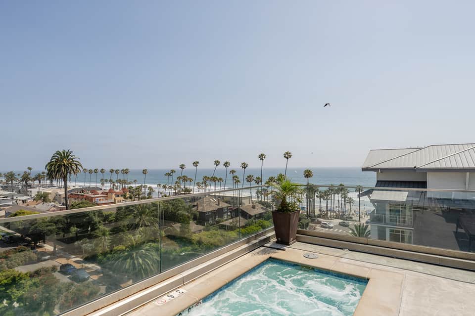 Oceanfront balcony with hot tub and palm trees lining the beach below