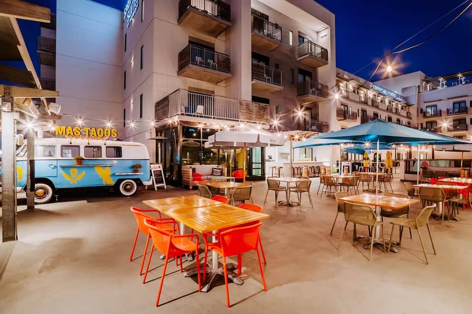 Outdoor dining area at night with colorful food truck, tables with umbrellas, and residential buildings