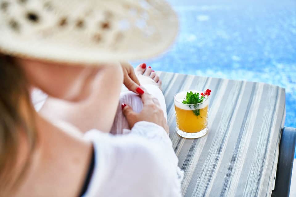 Woman's hand holding a tropical cocktail overlooking a bright blue swimming pool
