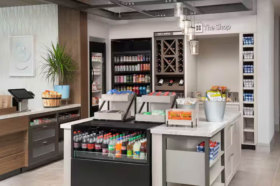 Modern hotel retail shop with beverage coolers, wine display, snacks, and checkout counter