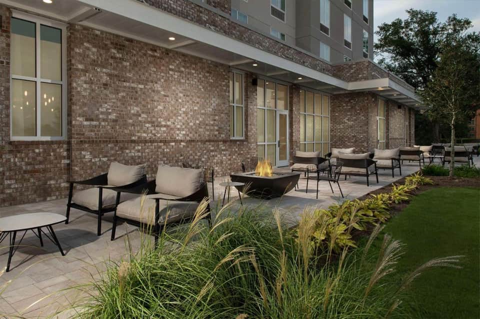 Modern outdoor patio with black lounge chairs, fire pit, and ornamental grasses against brick building