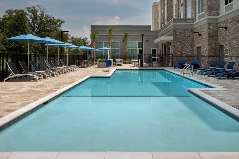 Resort swimming pool with blue umbrellas, lounge chairs, and modern brick building