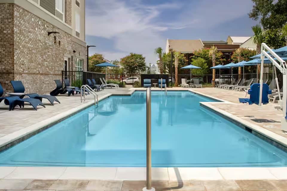 Resort lap pool with clear water, lounge chairs, umbrellas, and brick building