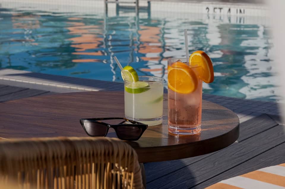 Refreshing cocktails with lime and orange garnish on wooden table by the pool