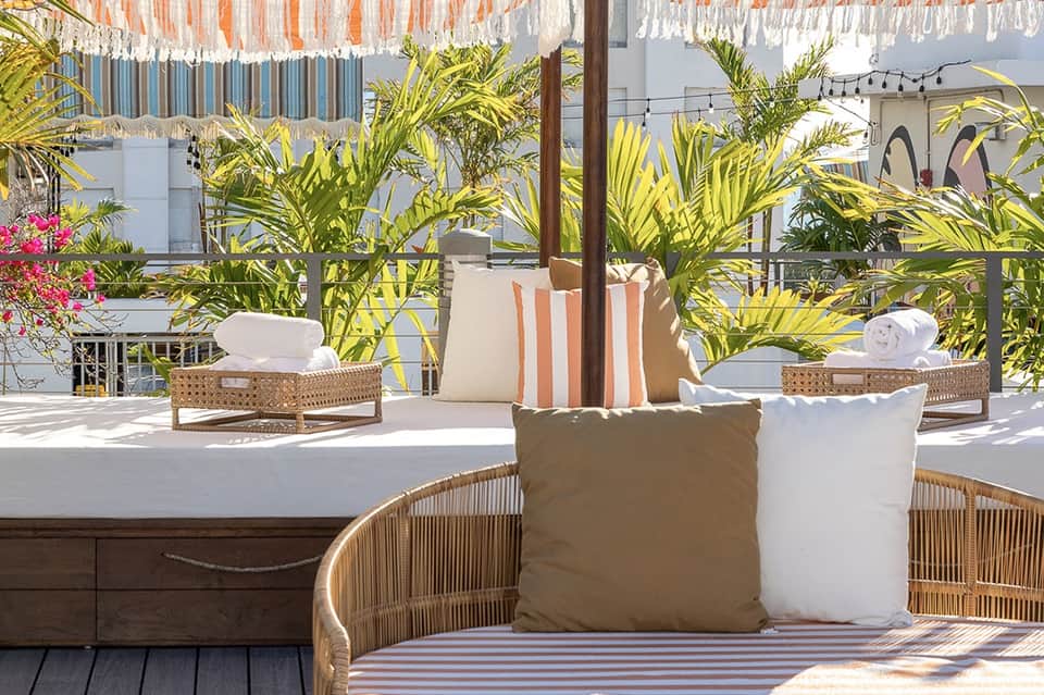 Covered patio seating area with wicker chairs, tropical plants, and striped cushions