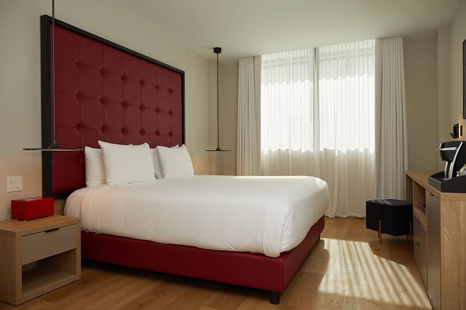 Contemporary bedroom with burgundy upholstered headboard, white bedding, wooden furniture, and sheer curtains