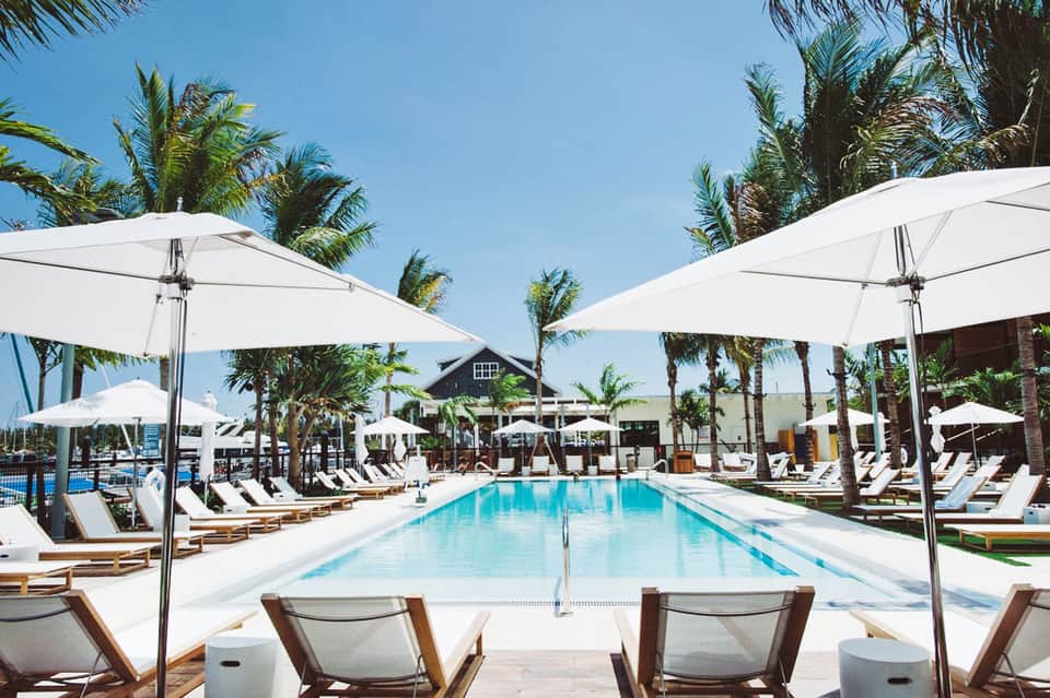 Luxury resort pool with white umbrellas, palm trees, and modern architecture under clear blue sky