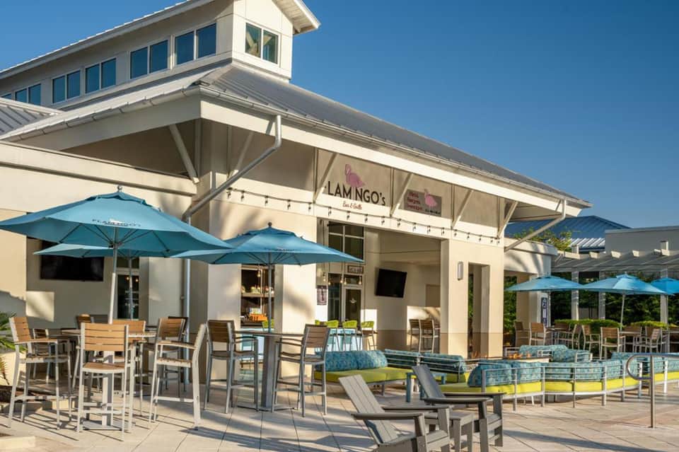 Outdoor patio with blue umbrellas, dining tables, and lounge chairs at a coastal resort cafe