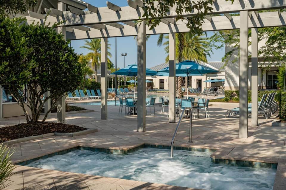 Spa hot tub under pergola with lounge chairs and pool area visible in background