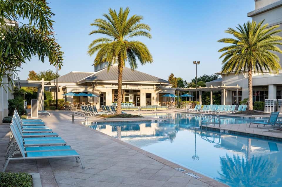 Resort pool area with palm trees, loungers, and white cabana building