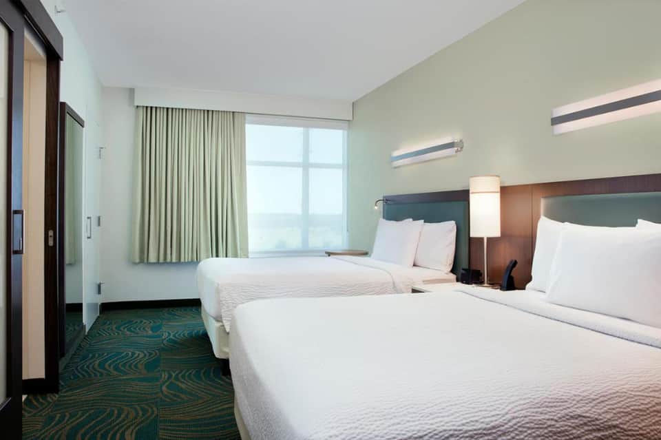Hotel room with two queen beds, green headboards, beige curtains, and ocean view from large window