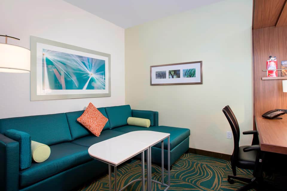 Hotel suite sitting area with teal sofa, coffee table, artwork, and wood accents