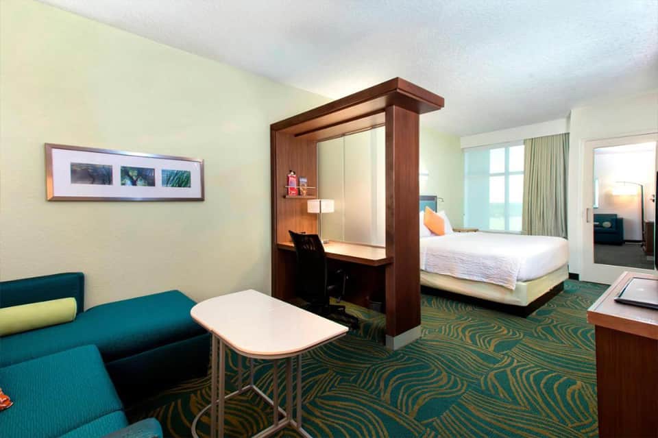Hotel suite with teal accents featuring living area, desk nook, and bed with patterned carpet