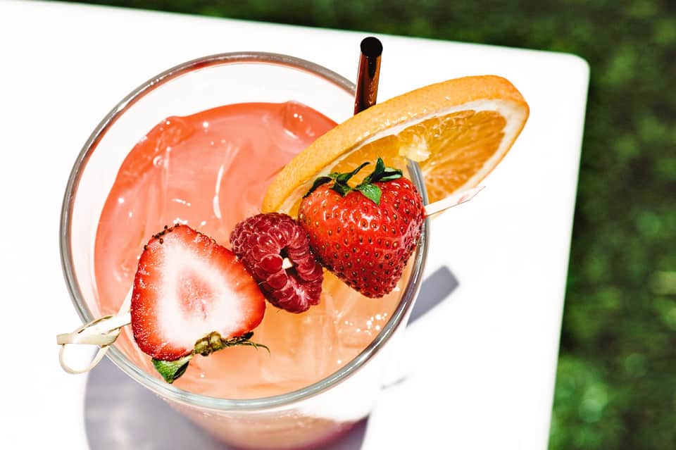 Colorful fruity cocktail garnished with fresh strawberries, raspberries, and orange slice
