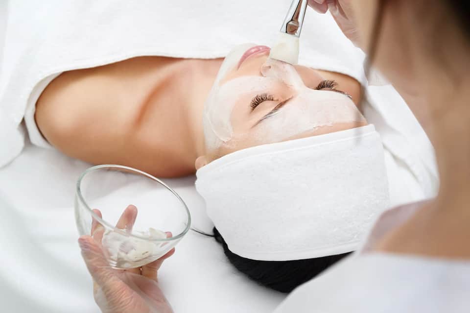 Facial spa treatment with esthetician applying mask to client's face