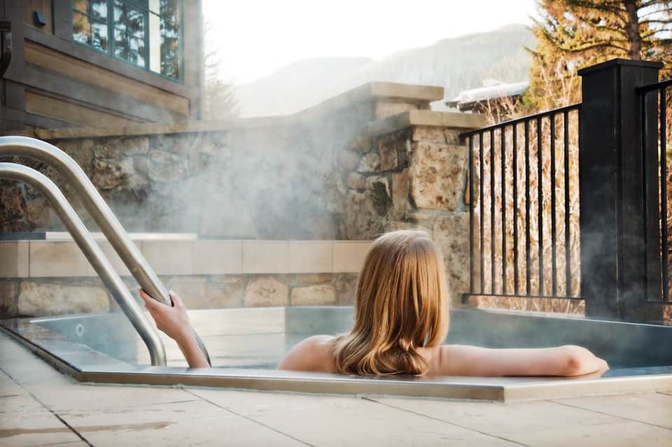 Woman relaxing in outdoor hot spring pool with mountain views and steam rising