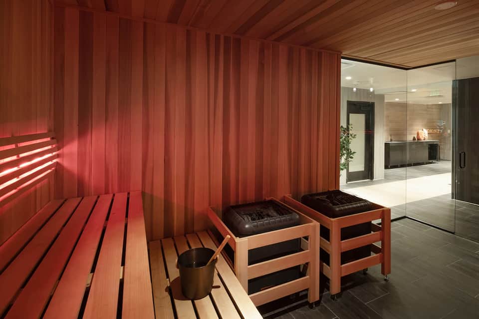 Modern sauna interior with red wooden walls, benches, and glass shower area with warm lighting