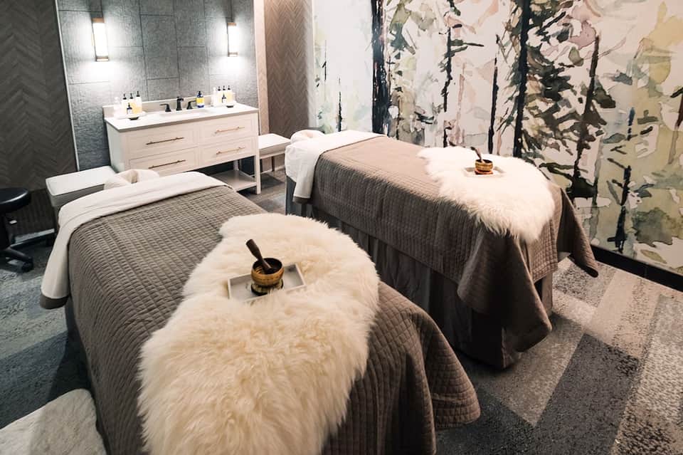 Spa treatment room with massage tables, white fur throws, and modern minimalist decor