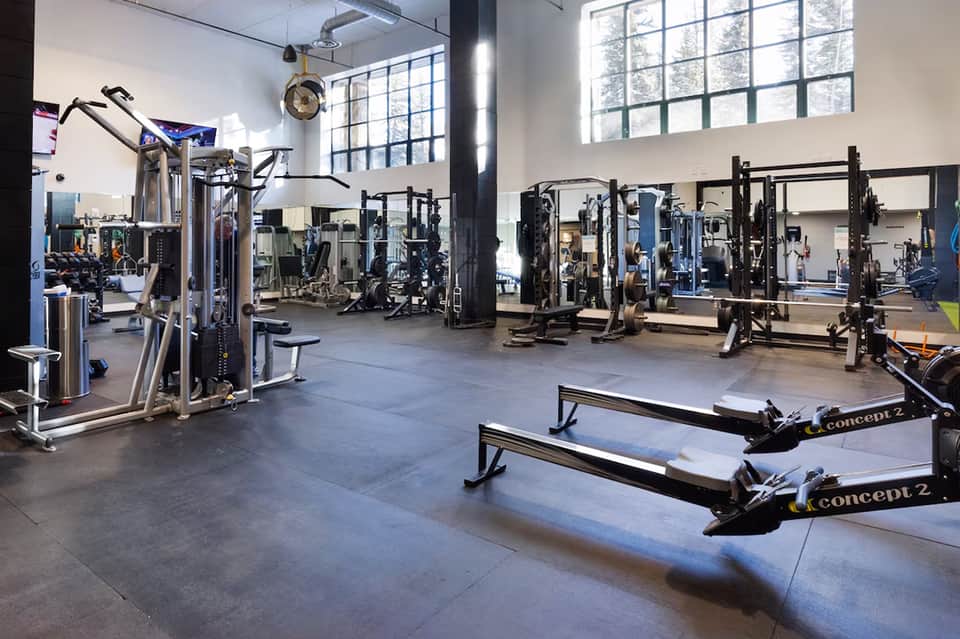 Modern fitness center with cardio machines, weight equipment, rowing machines, and large windows