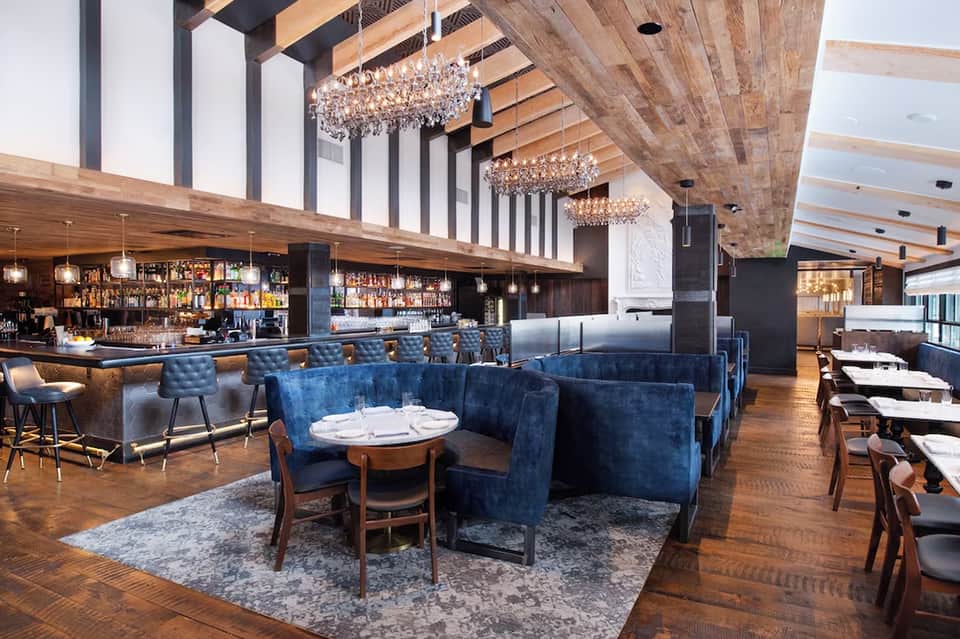 Modern restaurant interior with crystal chandeliers, blue velvet seating, and exposed wooden beams