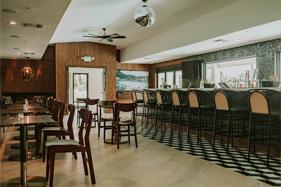 Upscale restaurant and bar interior with wood paneling, dark chairs, and geometric floor patterns