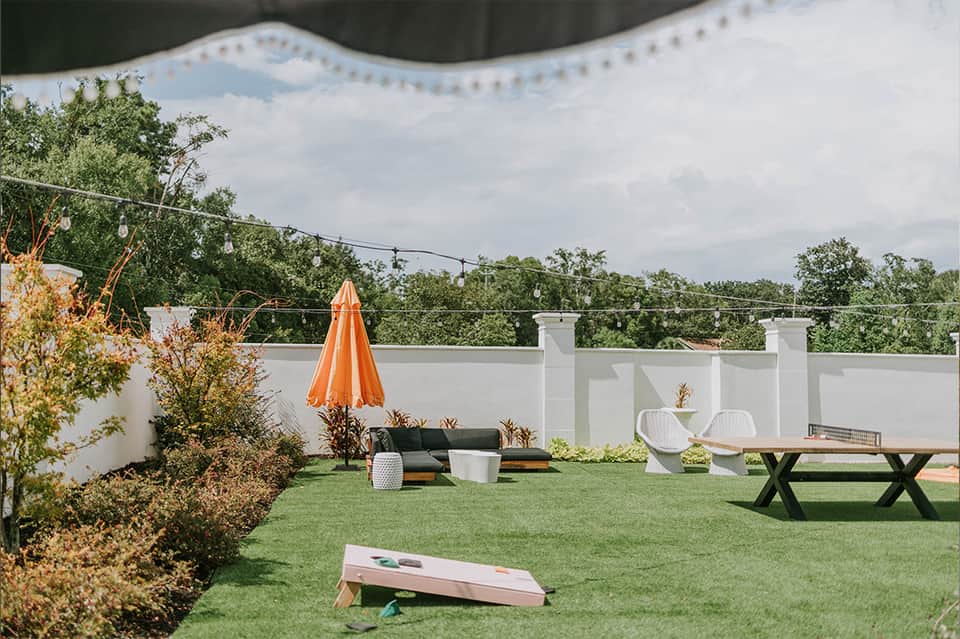 Rooftop lawn space with cornhole game, umbrella, seating, and white railings