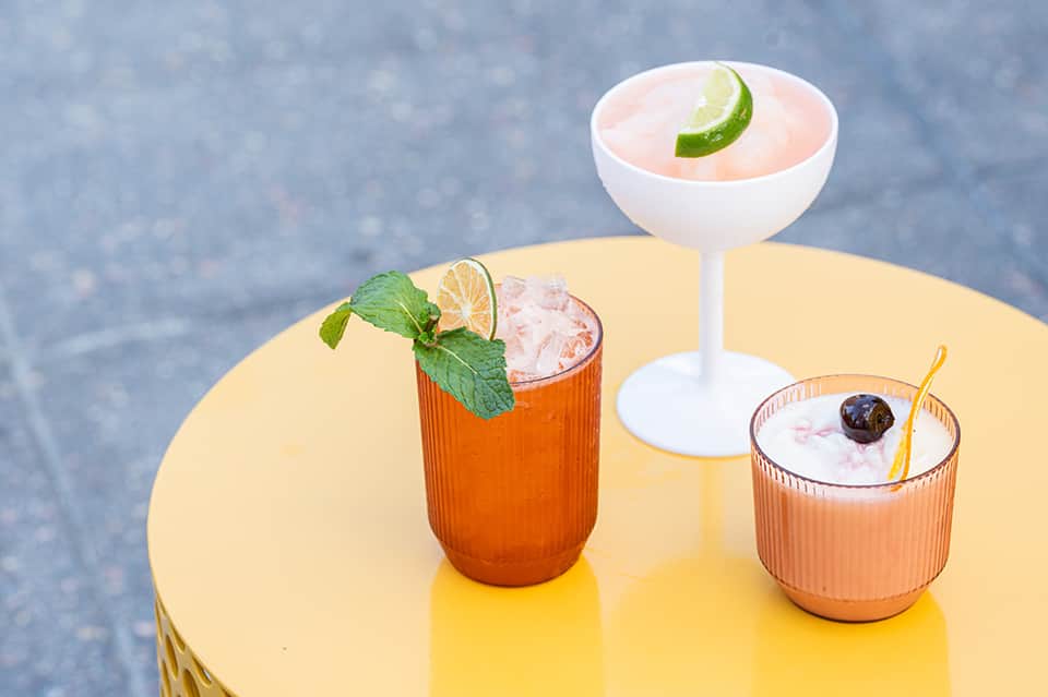 Colorful cocktails on yellow round table with mint garnish and blue water backdrop