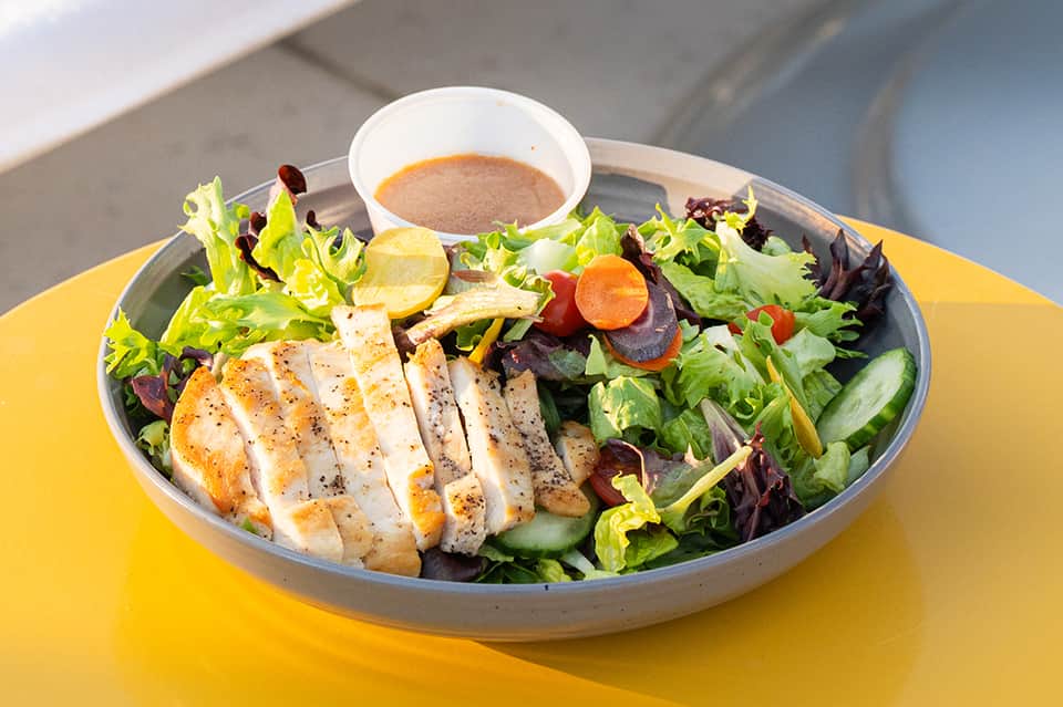 Grilled chicken salad with mixed greens and dressing on yellow poolside table