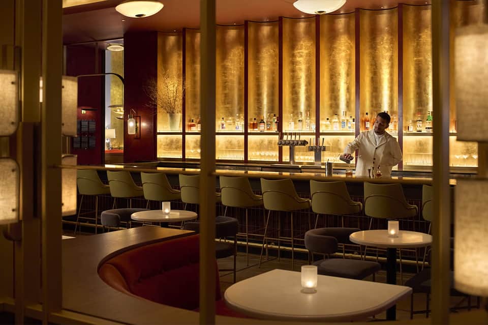 Upscale bar lounge with gold-lit wall display, modern seating, and bartender in white shirt