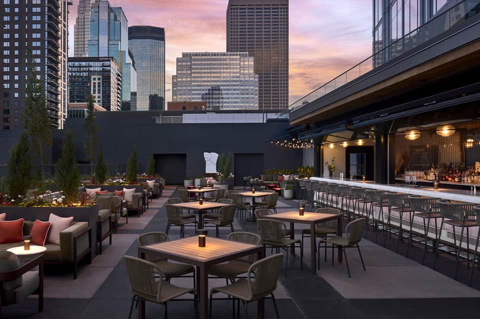 Modern rooftop bar and lounge at dusk with city skyline, seating areas, and ambient lighting