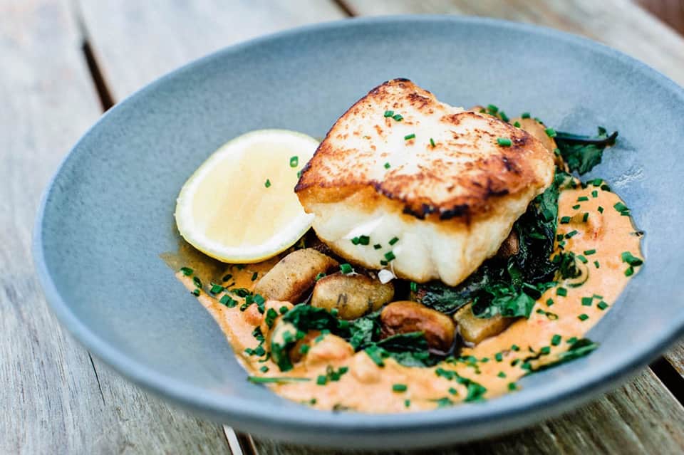 Seared fish fillet with lemon, mushrooms, and greens on blue plate
