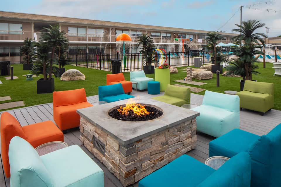 Outdoor resort courtyard with colorful modular seating around a fire pit, palm trees, and pool area