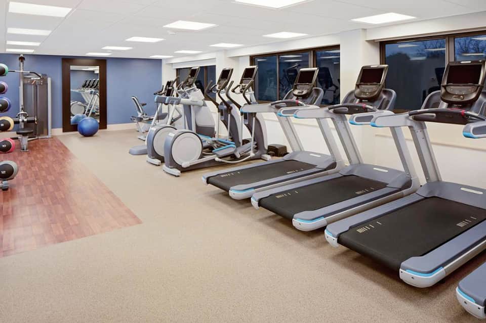 Modern fitness center with multiple treadmills, ellipticals, and exercise equipment under bright ceiling lights