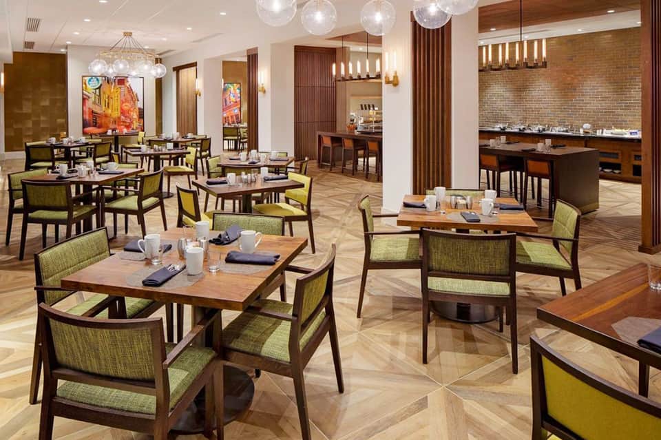 Modern dining room with wood tables, green chairs, and brick accent wall with pendant lighting
