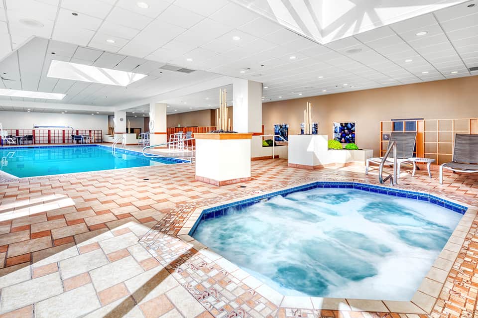 Indoor aquatic center with large swimming pool, hot tub, and relaxation seating areas under skylights